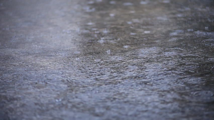 Raindrops splatter and form ringlets in the accumulated rainwater.