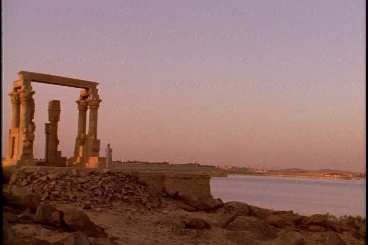 ASWAN, EGYPT - MAY 19,  1999: Scenic shots taken of islands in Lake Nasser; WS Temple of Het-Hert in late afternoon sun. A Nubian man stands next to the temple and bows in prayer.