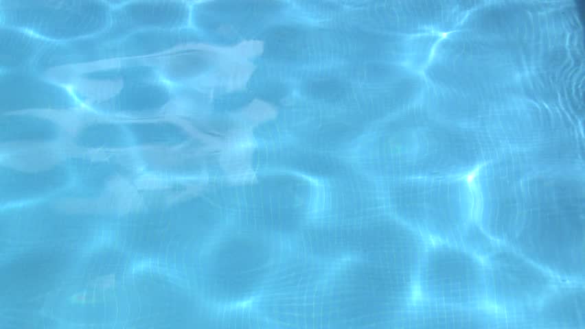 Clear blue private outdoor swimming pool, rippling water with caustics and blue tiled floor visible through water. Locked off shot.