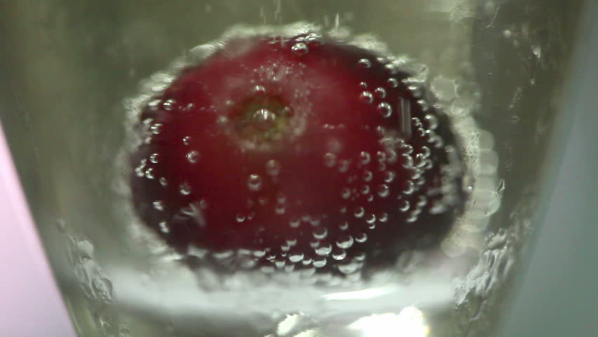 Red grapes falling into glass of golden bubbling champagne
