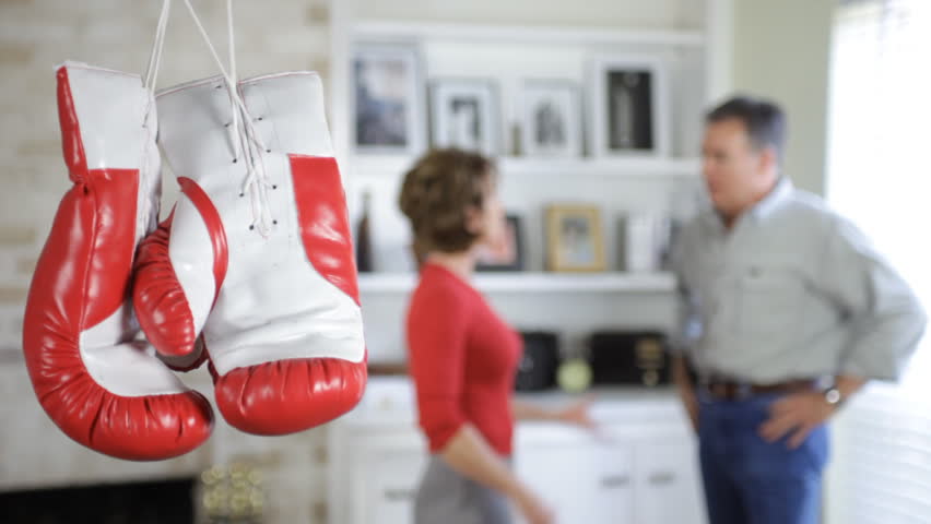 Boxing gloves hanging in the foreground, with a couple (out of focus) arguing in the background.