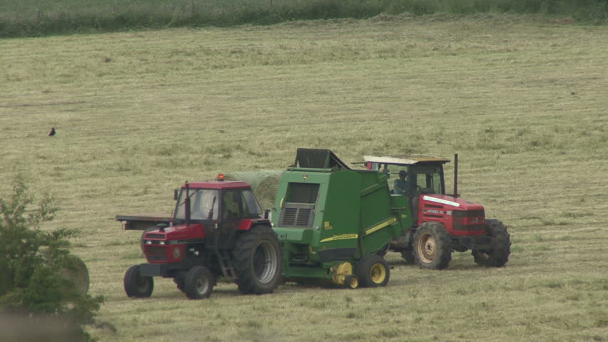 Hay baler ejects bale in front of tractor and trailer. HD.
