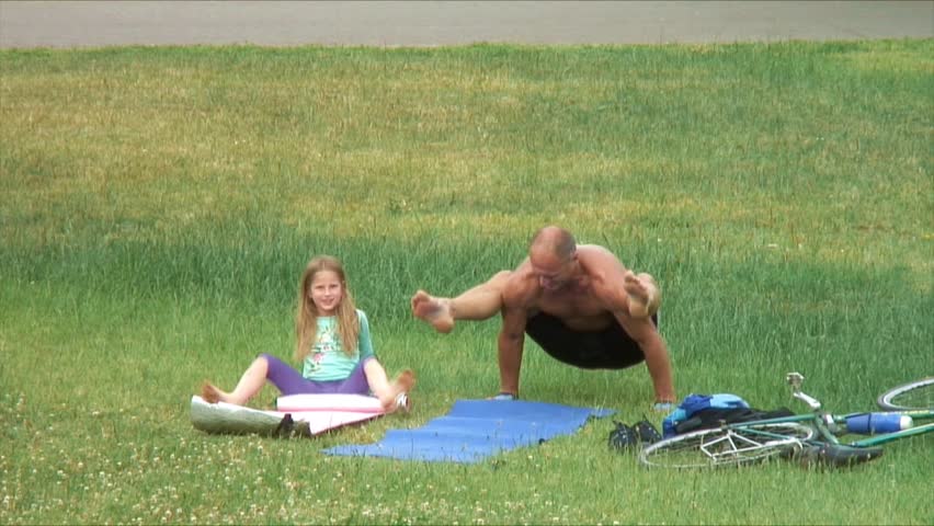 Mature man makes yoga in the park. Girl imitates him.