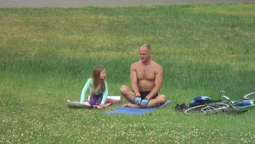 Mature man makes yoga in the park. Girl imitates him.