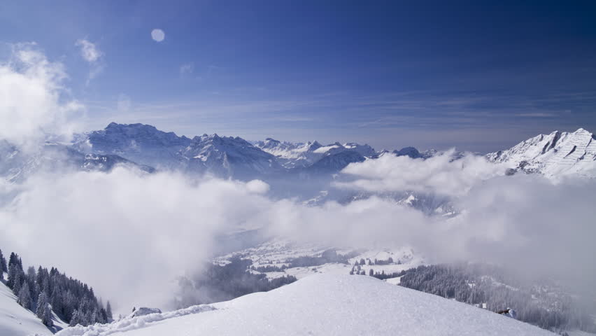Moving winter postcard: Snowy hills. Dramatic clouds form in a valley. View from the top of a mountain.