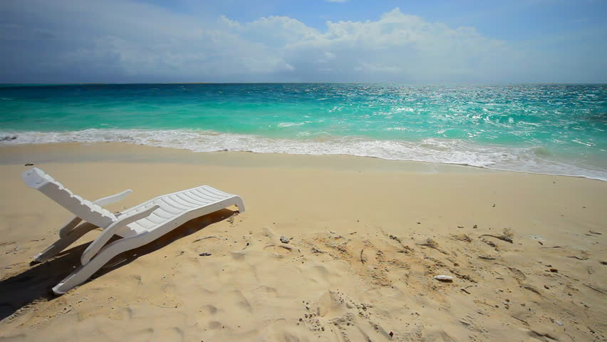 Unoccupied lounge chair wait for someone to sit in them on a sun drenched tropical beach. 