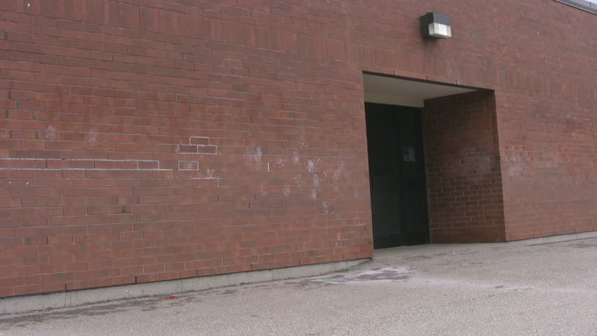 A man walks up to a red bricked school entrance, tries to open the door, finds it locked, and walks away.