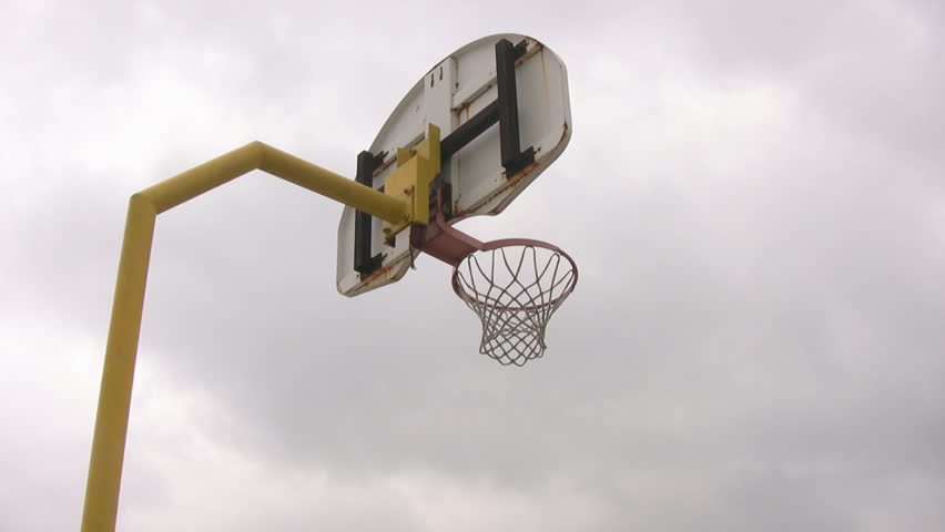 Looking up at an isolated outdoor basketball net, with an overcast, moody sky, moving in the background.