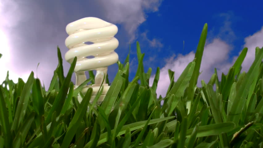 energy saving light-bulb in grass against timelapse of sky