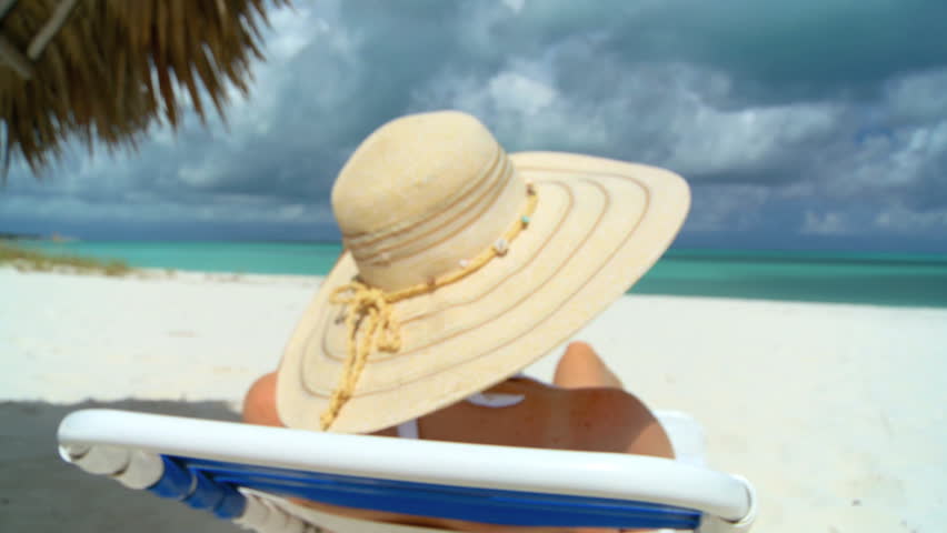 Elegant young female relaxing on white sandy beach looking at aquamarine waters