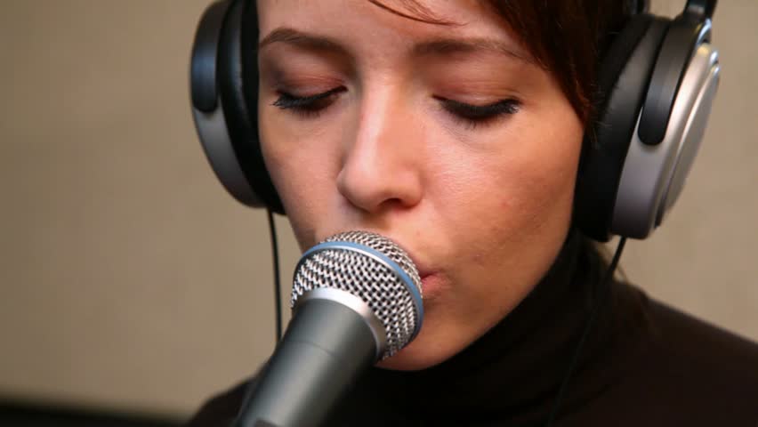 young woman singing through a microphone in studio 