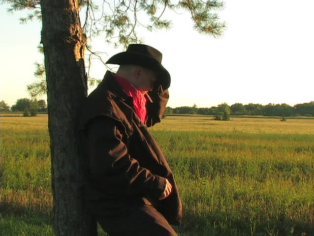 DOLLY IN TO A COWBOY SMOKING A CIGARETTE AS THE DAY'S LIGHT FADES.