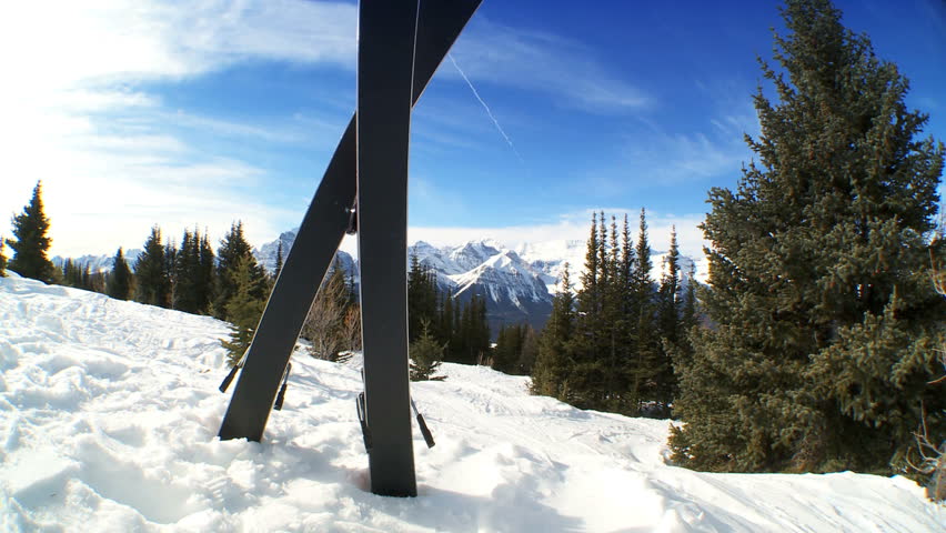 Crossed carver downhill skis & poles standing in fresh clean snow high in scenic mountain landscape