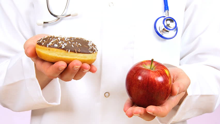 Doctor in white coat weighing up the choice between fresh fruit or sugary doughnut as a healthy food option