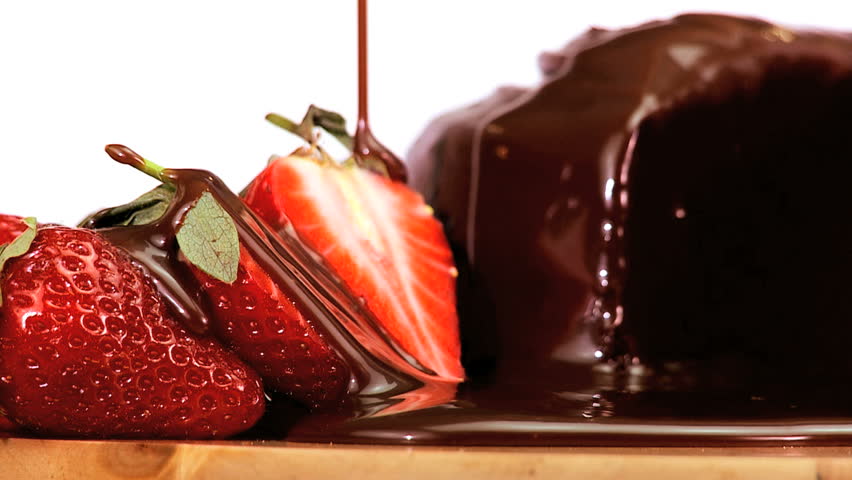 Indulgent chocolate cake & strawberries being covered in sweet sticky sauce on white background