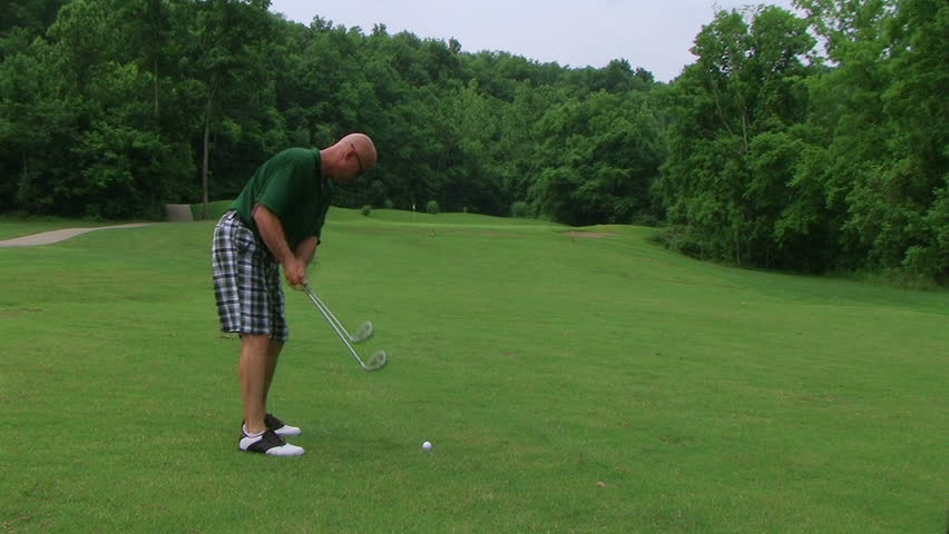 Golfer hitting ball with iron on fairway. 