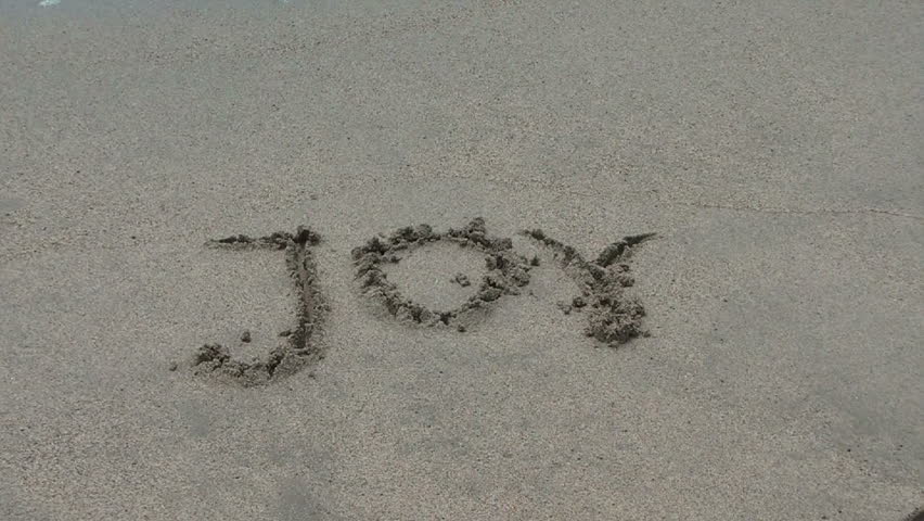 The water wipes off the word "joy" written in sand
