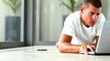 Smart young guy lying on floor browsing internet on laptop at home