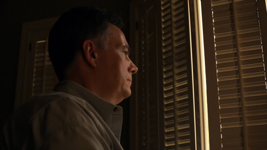 A man opens the shutters of a window and looks out at the sunshine and smiles.