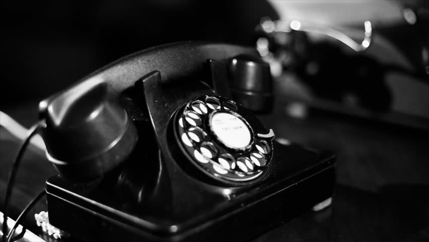 A woman picks up the receiver of an old vintage rotary style telephone and appears to be unable to get a dail tone. Film noir