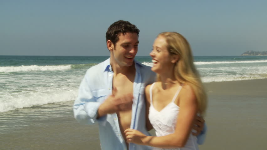 Young couple laughing while they walk along shore line at ocean