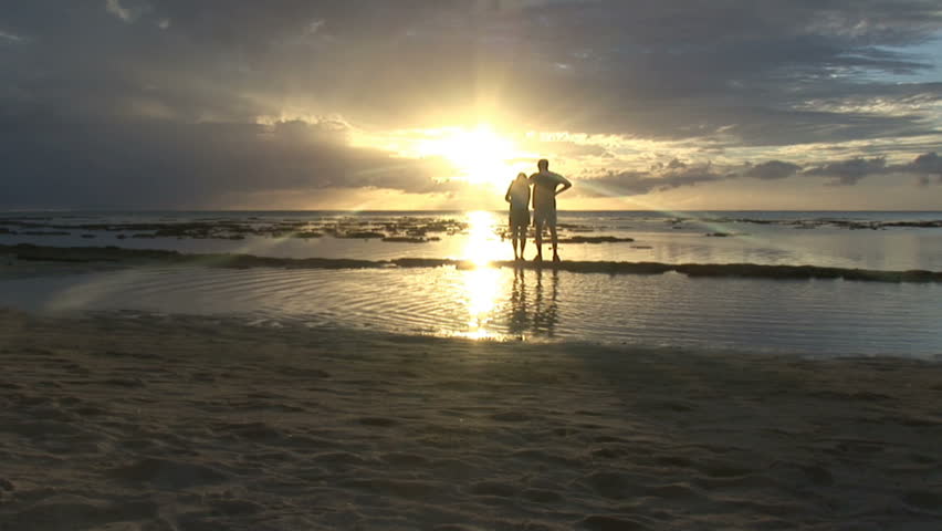 A couple watch the sunset on the shore of a tropical island