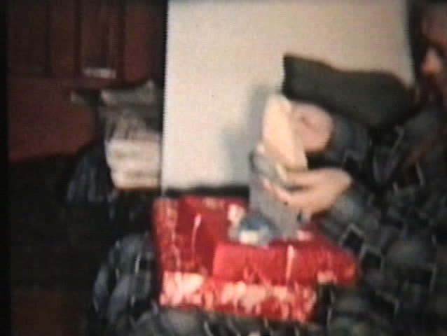 A family spend time together around the Christmas tree opening up gifts and presents to each other.