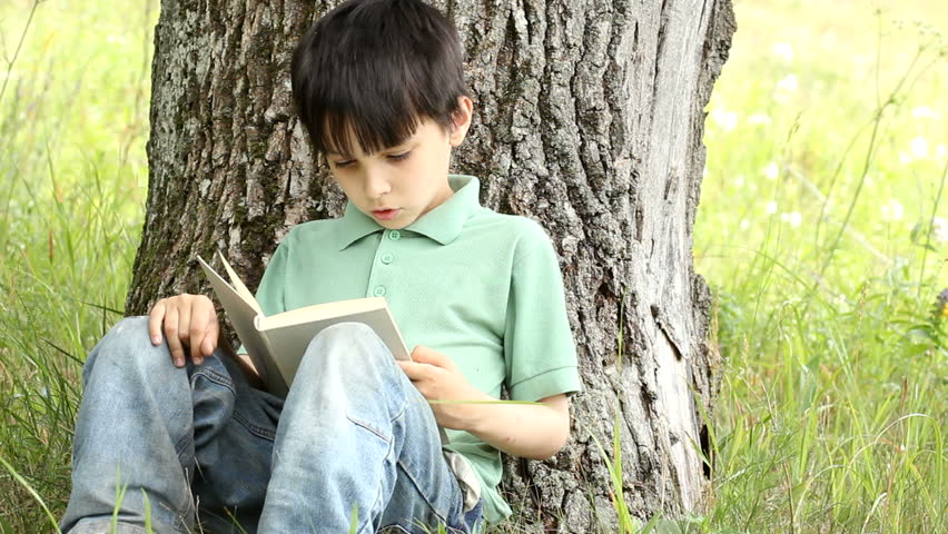 boy reads book outdoors.