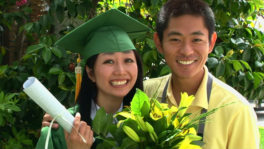 Young Asian woman in graduation gown with boyfriend outside 
