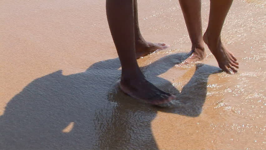 Young African American couple with feet in sand at beach-side