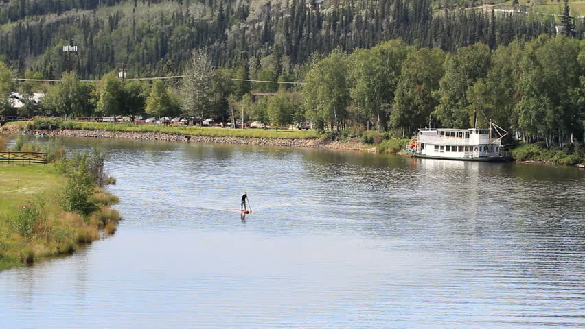 Float aircraft take off from river in Fairbanks, Alaska. Plane lifts from water and turns towards view. Old steam paddle boat on waters shore edge