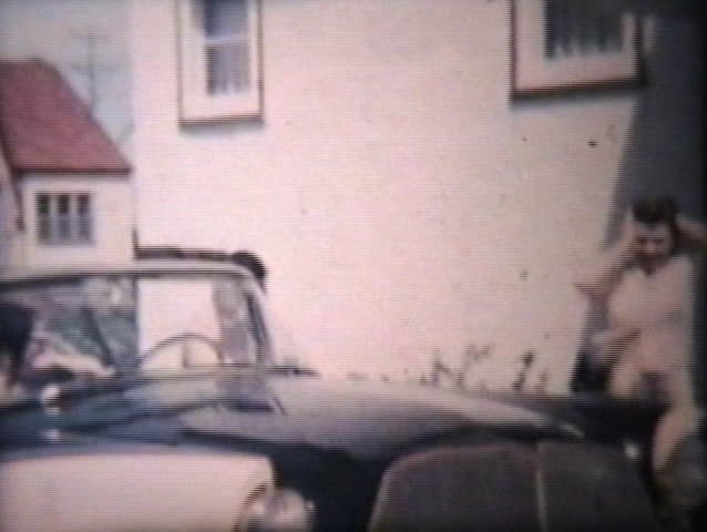 A happy newlywed couple finish packing up the old car and drive off to start their honeymoon together.