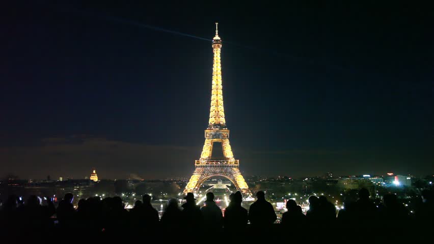 PARIS, FRANCE - JANUARY 2: Cars on crossroad under Eiffel Tower at night with silhouettes of tourists on January 2 2010 in Paris, France. The Eiffel Tower is the worldÃ¢â¬â¢s most visited paid monument.