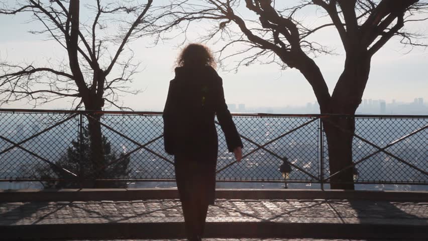 young woman walks up to railing at Mountmarte hill and looks at Paris.