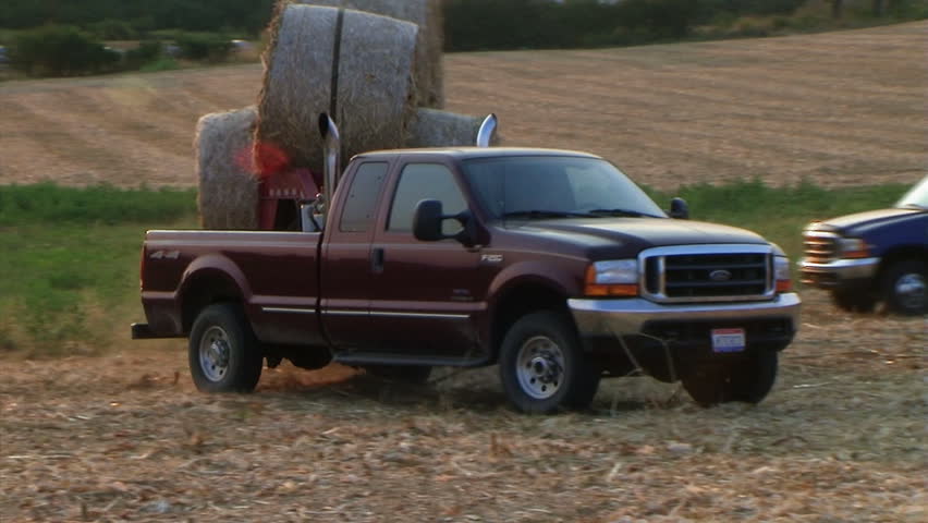 Trucks hauling round hay bales out of field - audio from external microphone. 