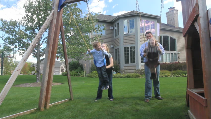 A father and mother push their two kids on the swings in the back yard of their luxury home 