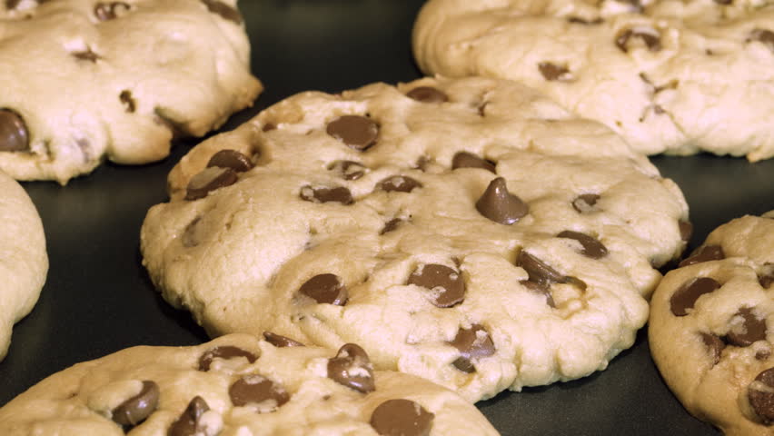 A zoom-in time lapse of chocolate chip cookies baking on a cookie sheet in an oven; progresses from raw dough to finished cookie (focus on one cookie).