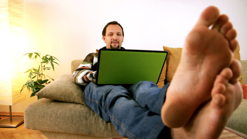 Man on sofa working on laptop barefoot