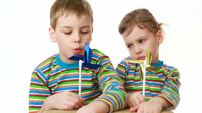 Little girl in a striped T-shirt with long sleeves and little boy in exactly T-shirt with a chocolate-smeared mouth sit at desk and blow into plastic propellers