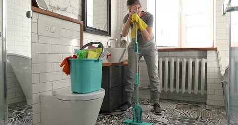 Woman is tired to cleaning tile in toilet. Woman holding a mop and cleaning floor in bathroom