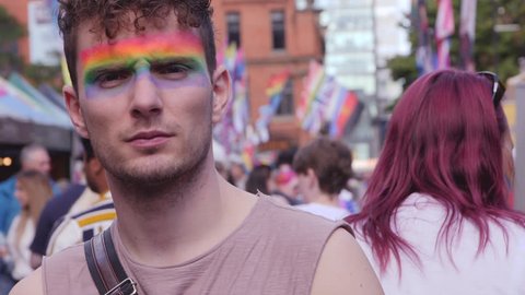 Pre Teenagers Lesbian - Guy with serious eyes and facepaint on at lgbtq pride, lesbian, gay,  bisexual, transgendered, queer, parade with rainbow flags and slow motion