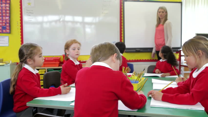 Female Pupil Stands At The Front Of Class With Teacher And Write On 