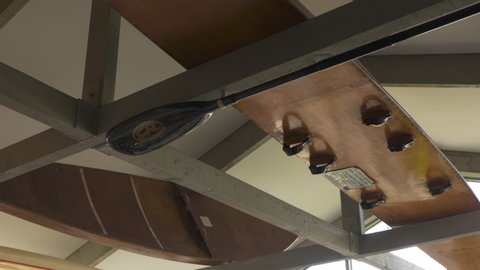 A Daylight Closeup Shot Of A Black Paddle And Pair Of Wooden Paddleboards Hanging In The Ceiling With Exposed Beams And Trusses