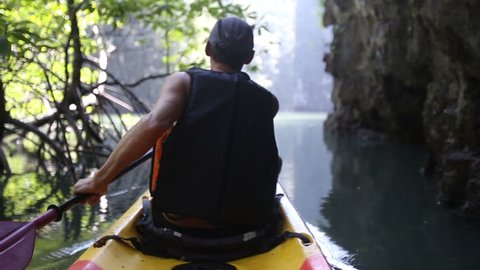 european man backside view in safity vest rows on kayak out of jungle to freshwater in canyon